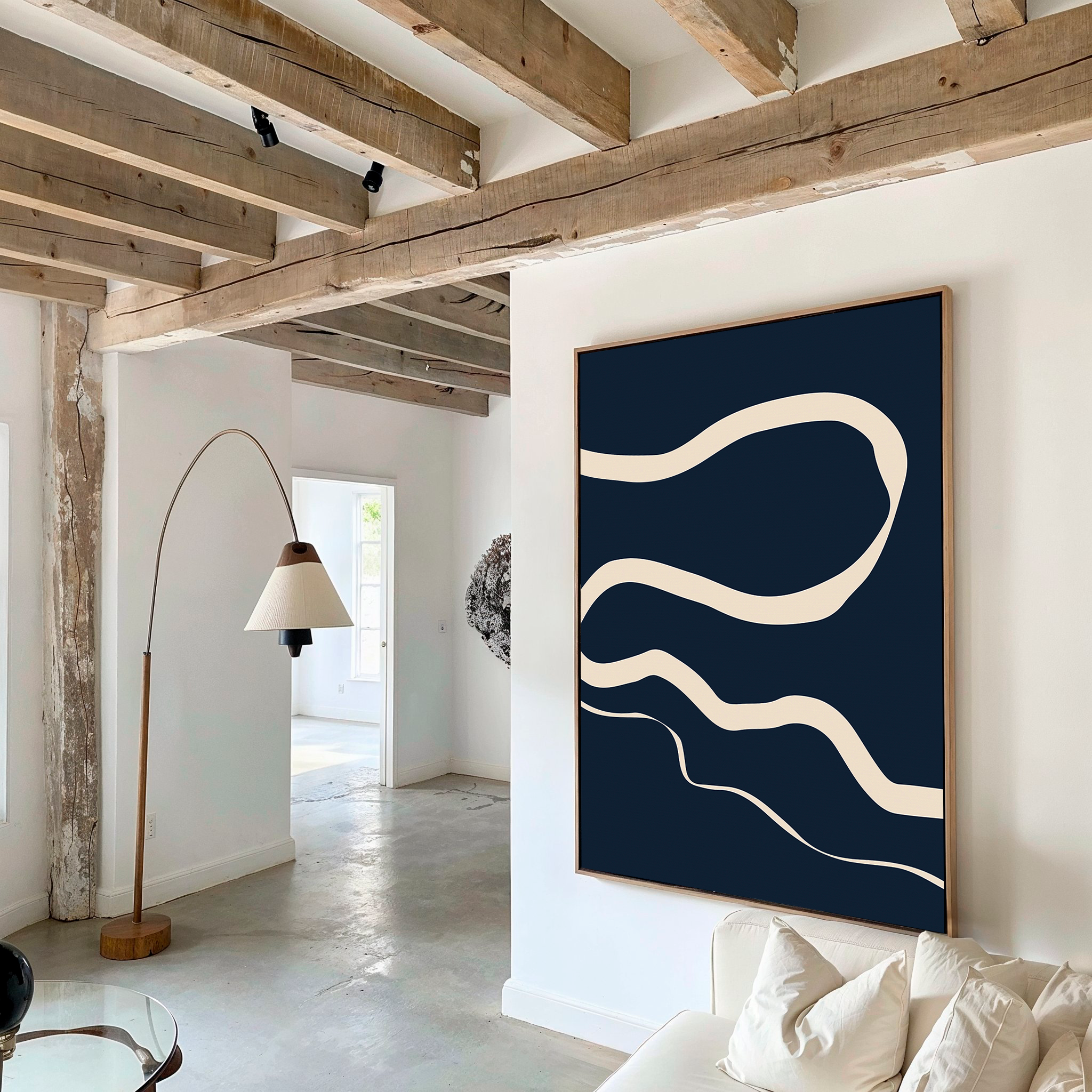A modern living room with exposed wooden beams, a white sofa, a curved floor lamp, and Blue Tranquility Abstract Canvas Art with cream wavy lines on a dark blue background as the focal point of the decor.