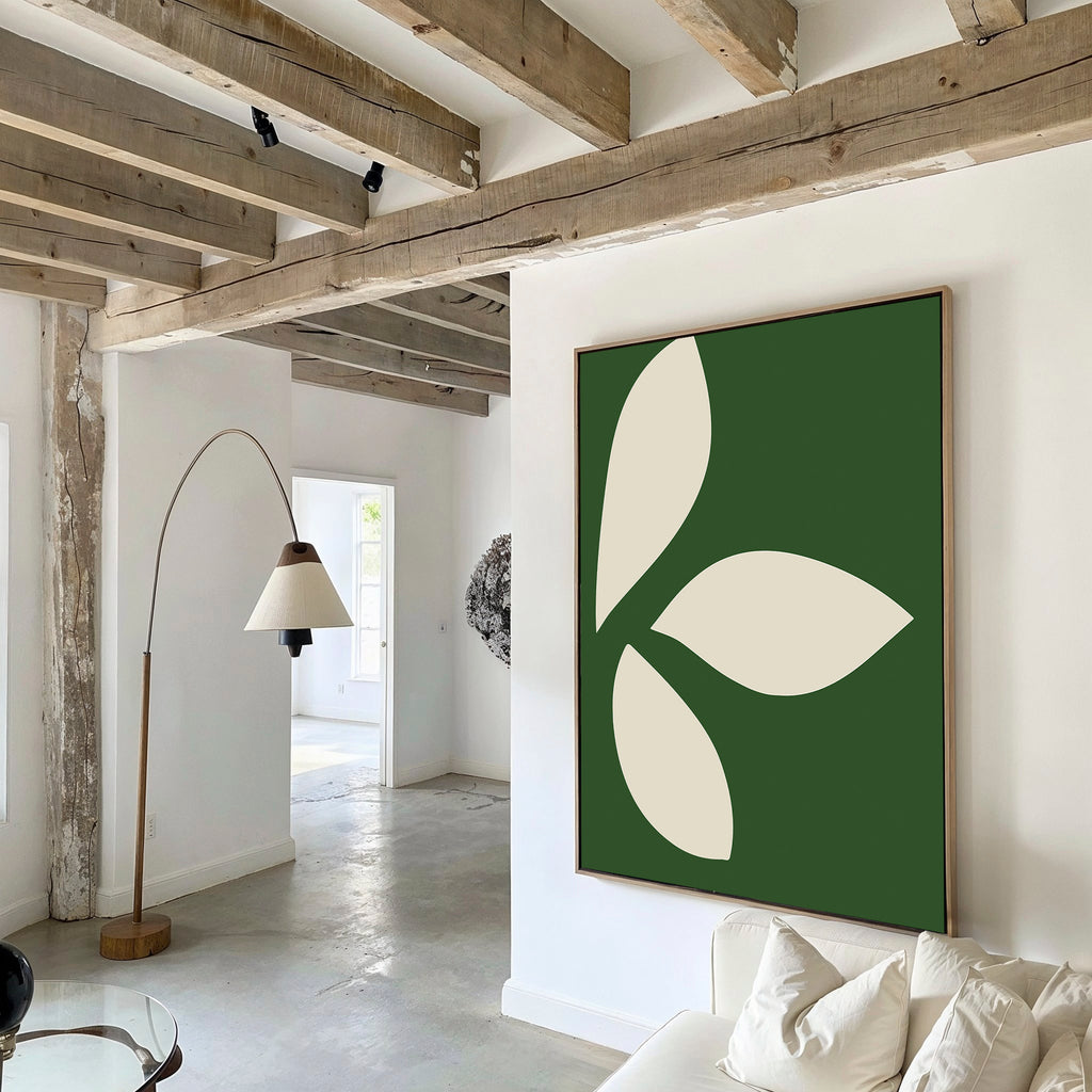 A modern living room features exposed wooden ceiling beams, white walls, and minimalist Leaf Silhouette Abstract Canvas Art—three cream leaf shapes on green. A curved floor lamp and a white sofa complete the elegant decor.