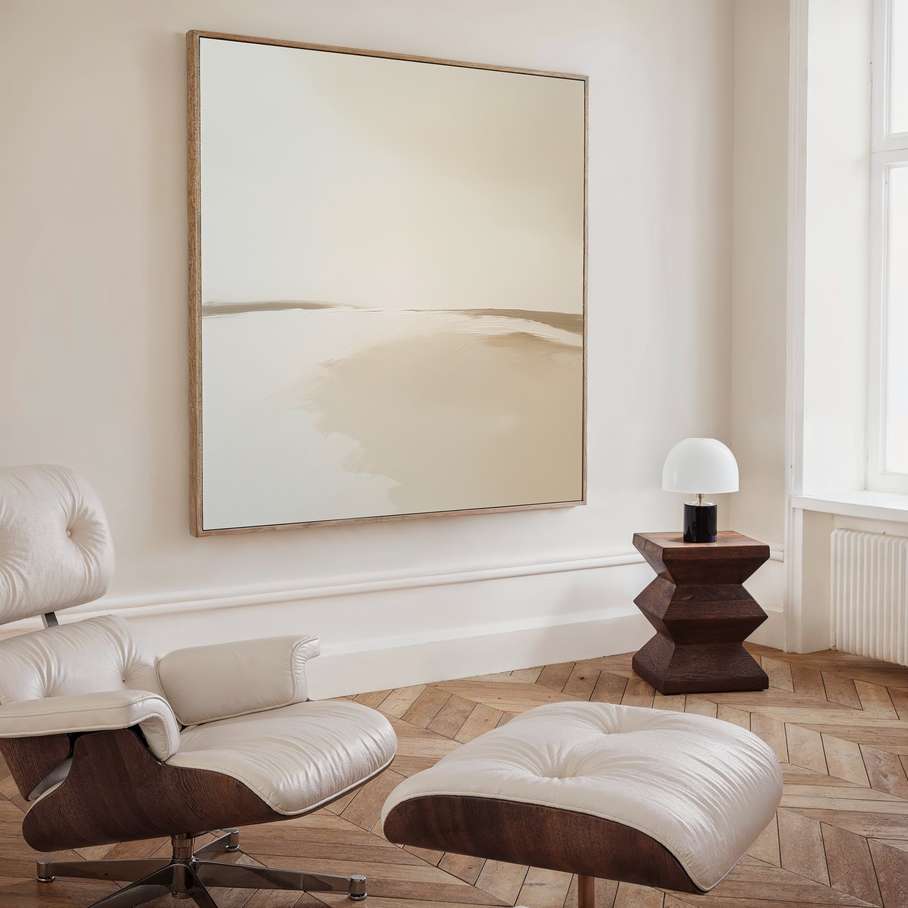 A modern, minimalist living room features a white leather lounge chair and ottoman, a geometric wooden side table with a lamp, and the Serene Expanse Abstract Canvas Art by My Store in soft beige tones enhancing the decor.