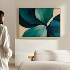 A person in white admires the Lush Teal Foliage Abstract Canvas Art—a large artwork of green and blue leaves on beige—displayed above a light sofa, enhancing the modern living room decor.