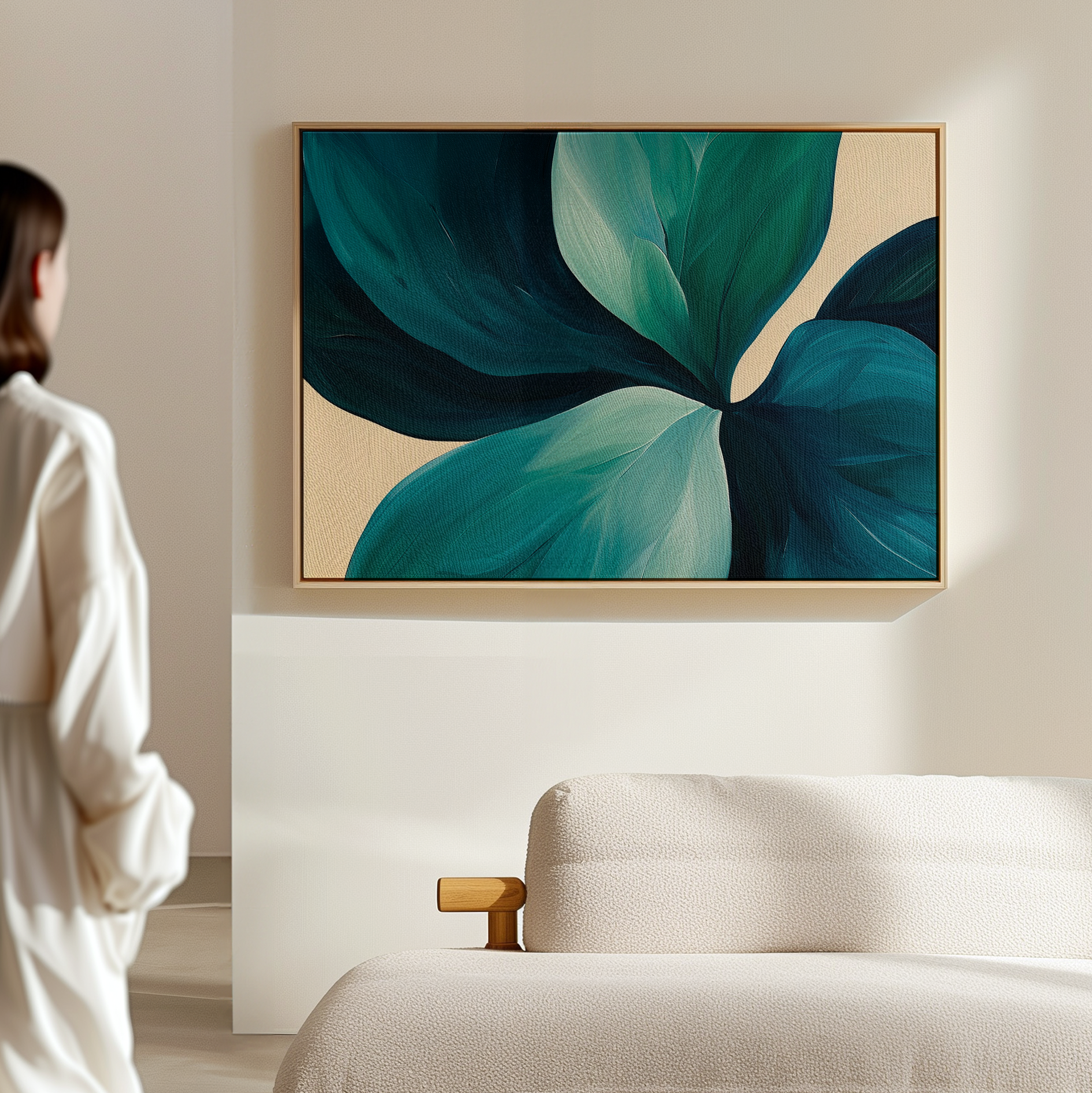 A person in white admires the Lush Teal Foliage Abstract Canvas Art—a large artwork of green and blue leaves on beige—displayed above a light sofa, enhancing the modern living room decor.