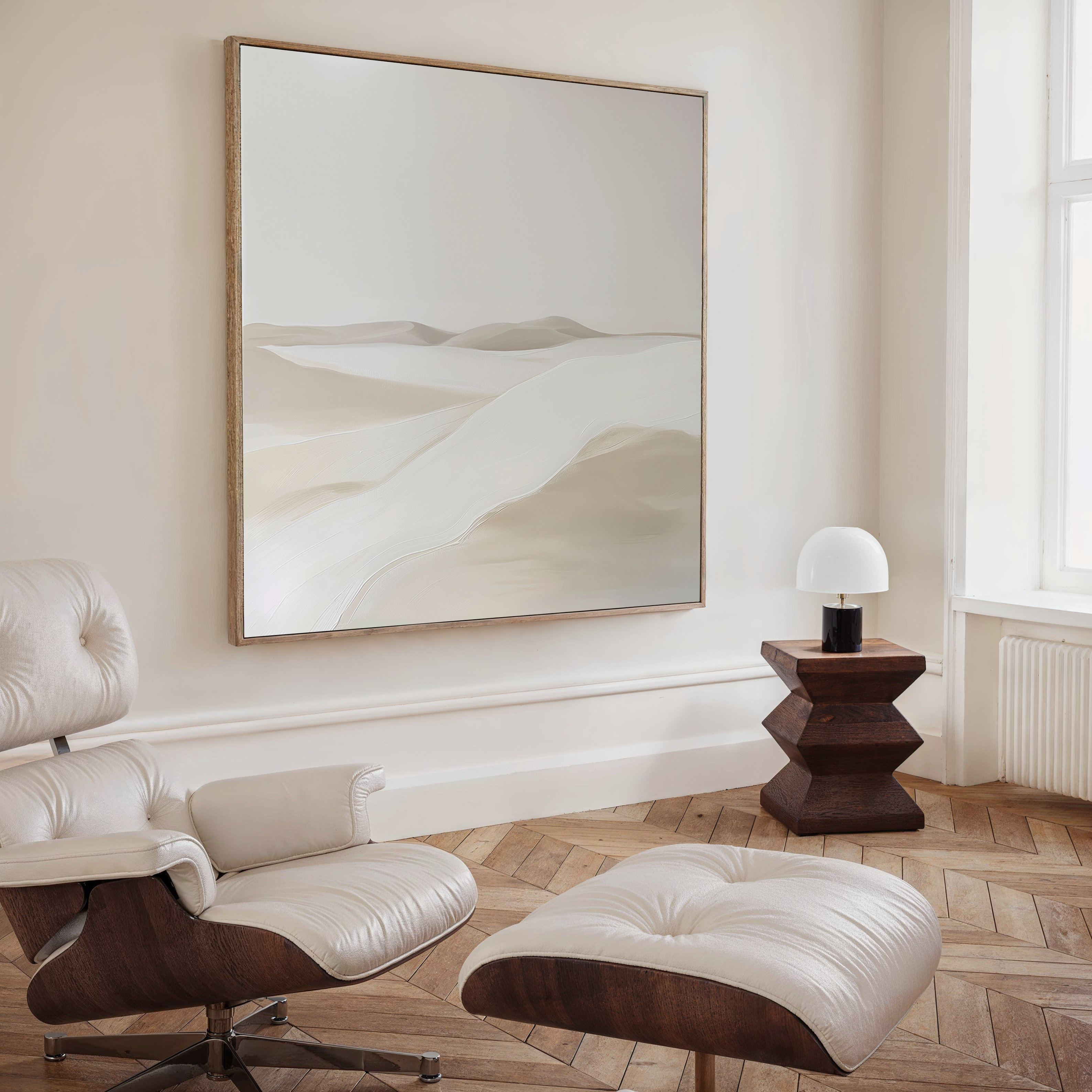 A minimalist living space featuring the Misty Vale Abstract Canvas Art—a striking large desert painting—paired with a white and wood lounge chair, geometric wooden side table, and a small white lamp by the window for effortless decor.