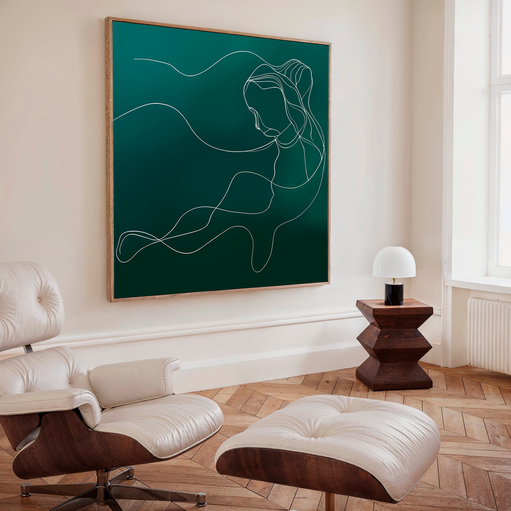 A modern living room features a white lounge chair and ottoman, a wooden side table with lamp, and the Azure Silhouette Abstract Canvas Art—a striking minimalist piece of a woman on dark green—creating sophisticated decor.