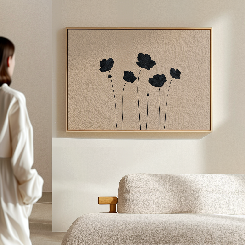 A woman in a white robe stands in a minimalistic living room, admiring the Botanic Abstract Canvas Art above a textured cream sofa. The artwork features black, abstract floral silhouettes on a light beige background.