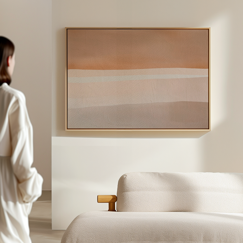 A person stands in a softly lit, minimalist room with a beige couch and the Saharan Lines Abstract Canvas Art—a large, warm-toned, desert-inspired painting—hanging on the wall.