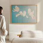 A person in a white shirt stands by a beige sofa, admiring the Stellar Flora Abstract Canvas Art—three white flowers on a soft blue background—highlighted in a sunlit, minimalist living room.