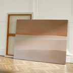 Two large canvases rest against a white wall on a wooden herringbone floor; one is backward, while the other displays the Saharan Lines Abstract Canvas Art with soft beige, brown, and cream horizontal bands inspired by desert landscapes.