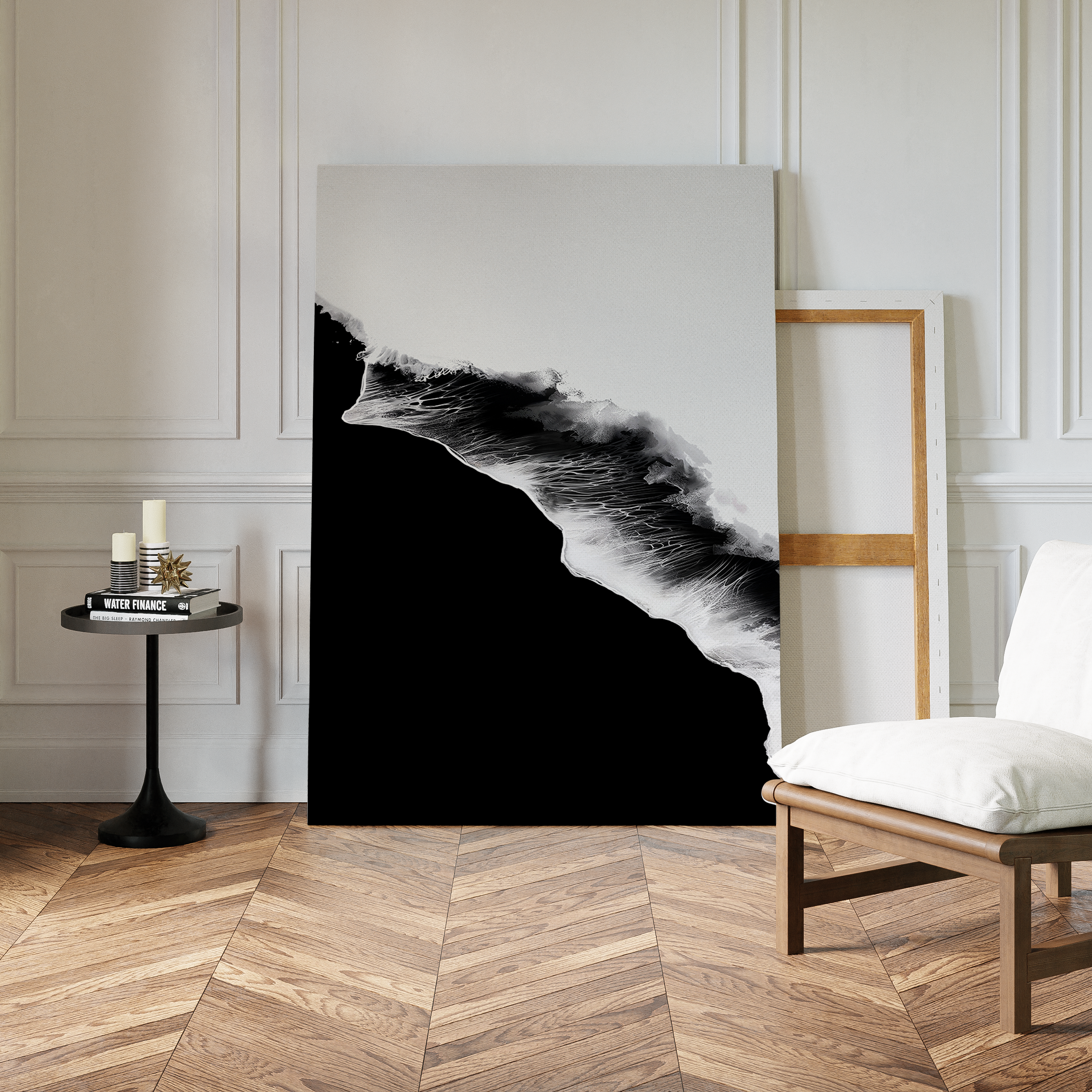 A modern room with chevron wood flooring features the Black Ocean Abstract Canvas Art propped against a wall in a wooden frame, alongside a white cushioned chair and a small black table with candles and books.