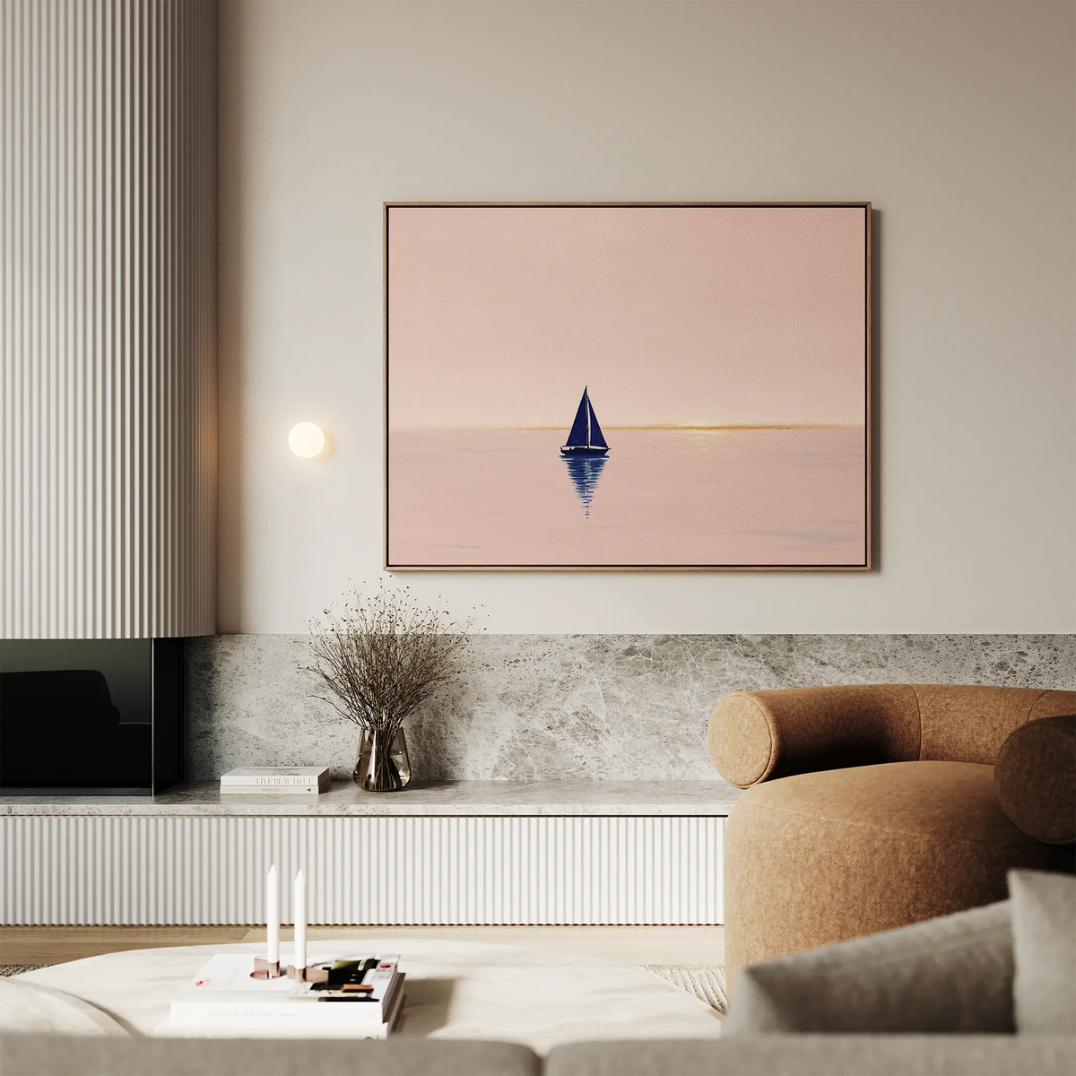 A modern living room with neutral tones features calming wall art—the Rose Harbor Canvas Art, showing a blue sailboat at sunset—mounted above a marble shelf with minimalist decor and a beige curved sofa.