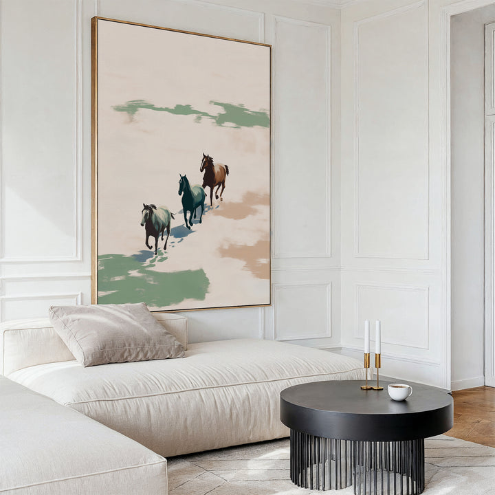 A modern living room with a light beige sectional, a round black coffee table, and the Running Free Canvas Art displaying three horses in muted green and brown tones, creating a minimalist vibe.
