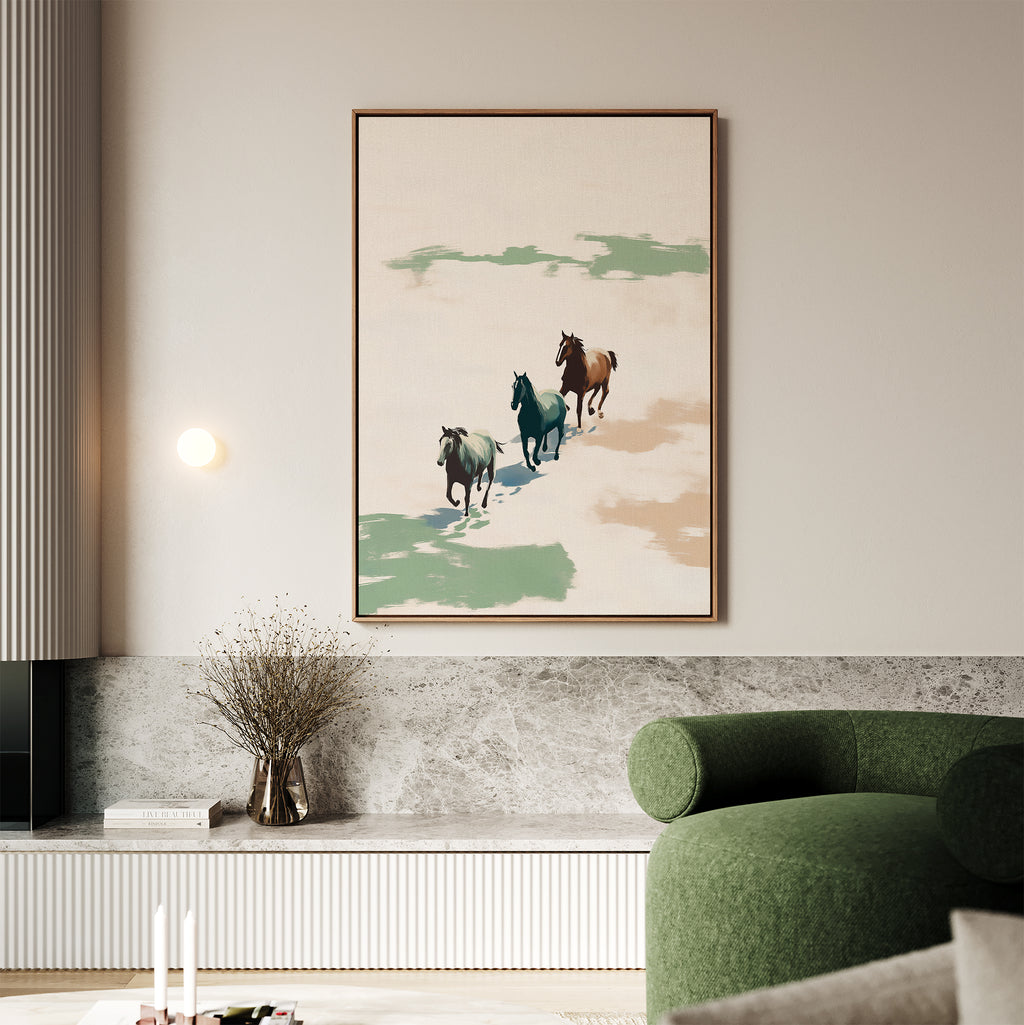 A modern living room showcases the Running Free Canvas Art, a large abstract landscape print of three horses, above a marble bench with dried flowers. A green curved sofa sits in front; minimalism and soft neutrals set the tone.