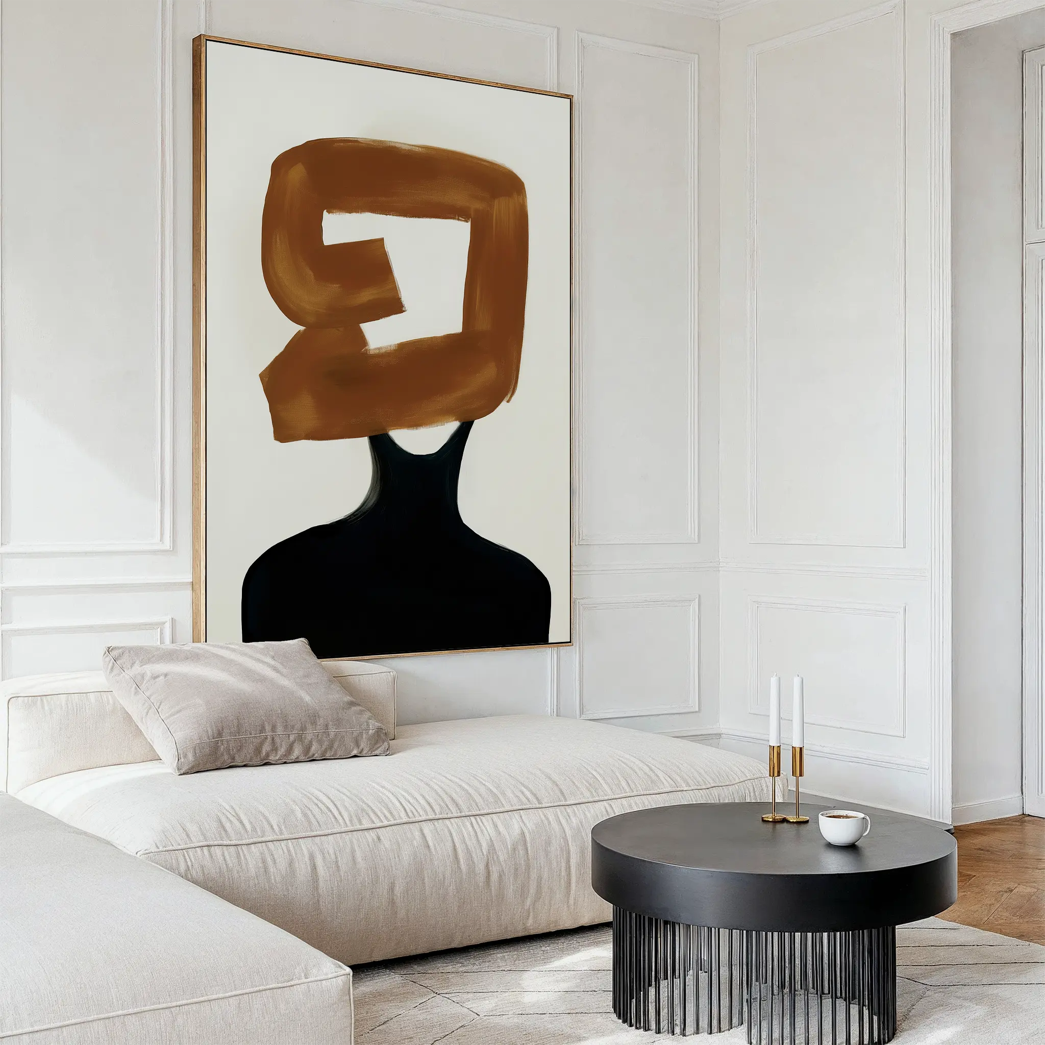 A modern living room with a cream sofa, round black table, two candlesticks, a cup, and the Rustic Persona Canvas Art—abstract wall art featuring a headless black form with bold brown brushstrokes on a minimalist background.