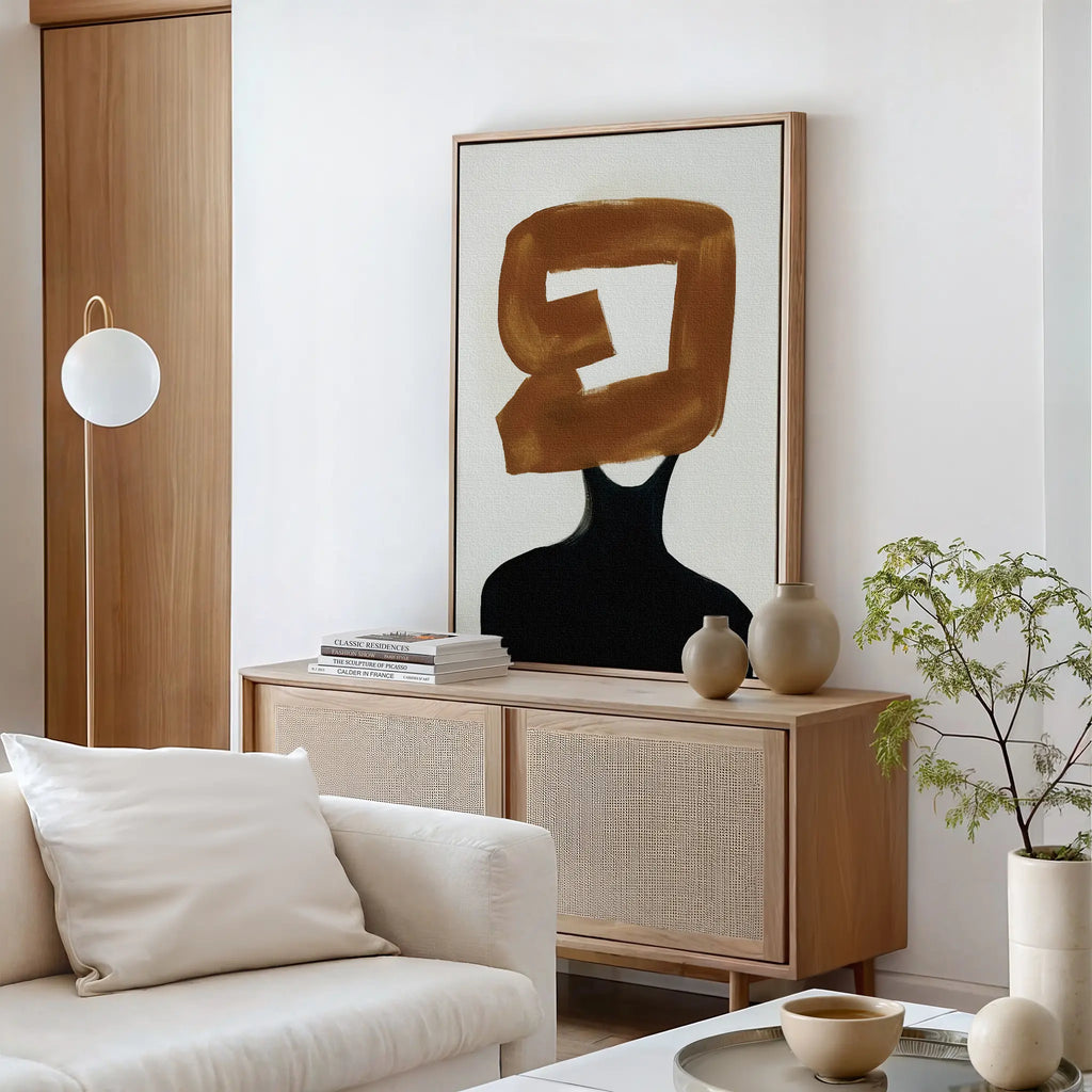 A modern living room features a light sofa, wooden sideboard, potted plant, ceramic decor, and the Rustic Persona Canvas Art—an abstract wall piece showcasing a gold brushstroke over a black figure for a striking silhouette.
