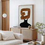 A modern living room features a light sofa, wooden sideboard, potted plant, ceramic decor, and the Rustic Persona Canvas Art—an abstract wall piece showcasing a gold brushstroke over a black figure for a striking silhouette.