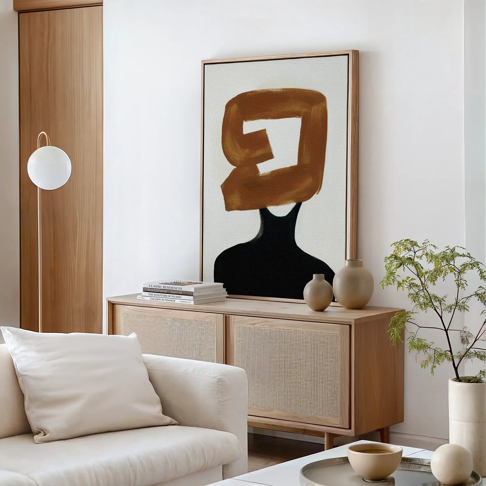 A modern living room features a light sofa, wooden sideboard, potted plant, ceramic decor, and the Rustic Persona Canvas Art—an abstract wall piece showcasing a gold brushstroke over a black figure for a striking silhouette.
