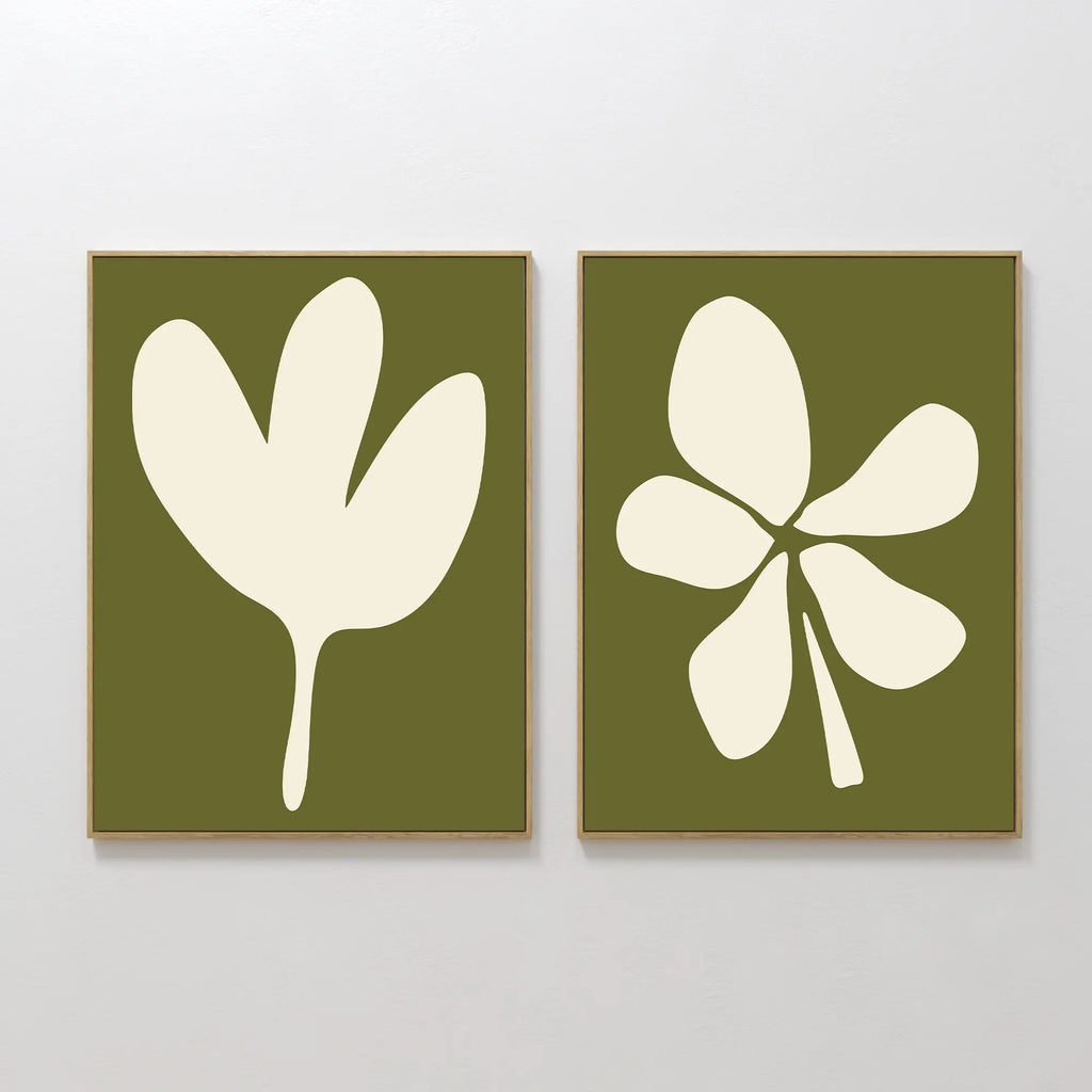 The Sage Petal Set of 2 features minimalist wall art prints with sage green backgrounds and white floral silhouettes, each framed in light wood and displayed side by side on a white wall.