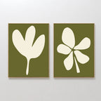 The Sage Petal Set of 2 features minimalist wall art prints with sage green backgrounds and white floral silhouettes, each framed in light wood and displayed side by side on a white wall.