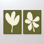 The Sage Petal Set of 2 features framed minimalist wall art prints with abstract white leaf and floral silhouettes on sage green backgrounds, displayed side by side on a light-colored wall.