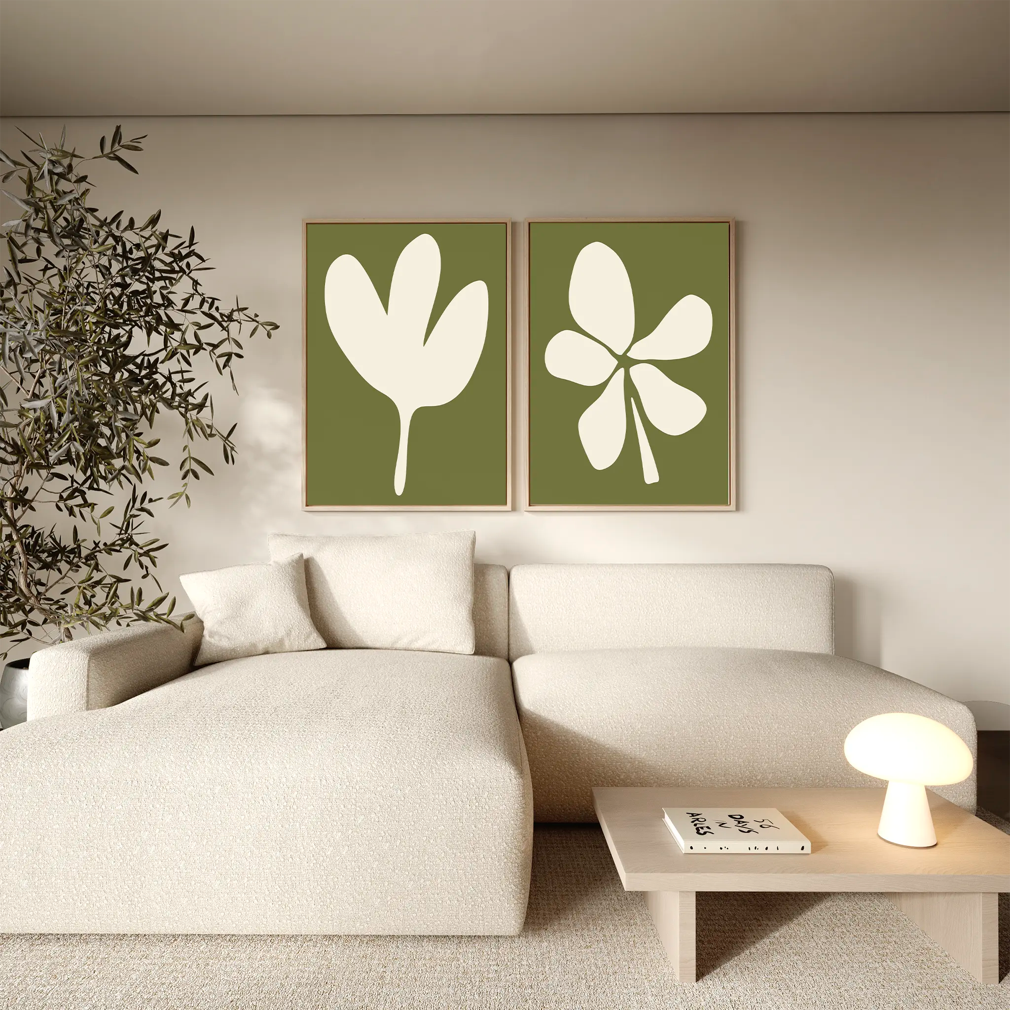 A modern living room features a beige sectional, wooden coffee table with a lamp and books, leafy plant, and the Sage Petal Set of 2—abstract floral wall art prints on an olive or sage green background.