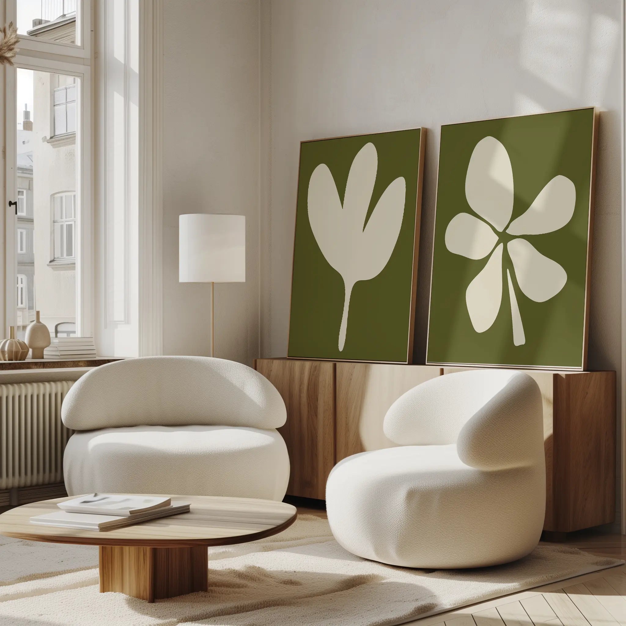 A modern living room features two white rounded armchairs, a low wooden coffee table, a floor lamp, and the Sage Petal Set of 2 floral wall art prints on the console. Sunlight streams through tall windows.