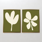 The Sage Petal Set of 2 features framed minimalist wall art prints with abstract white floral silhouettes and unique leaf designs on sage green backgrounds, displayed side by side on a light-colored wall.