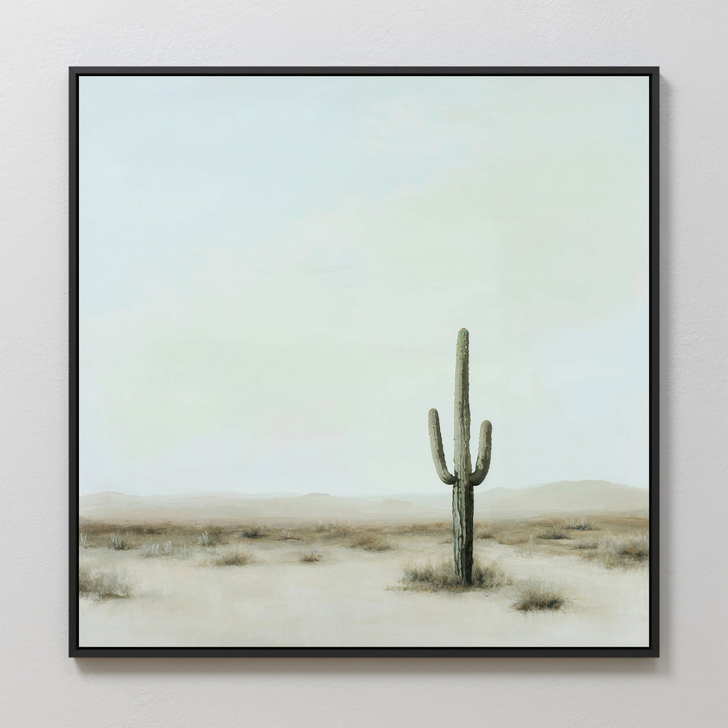 Elevate your modern space with the Saguaro Whisper Canvas Art—minimalist wall art showcasing a lone saguaro cactus in a vast desert beneath a cloudy sky, framed in black and hung on a light wall. Perfect as a large statement piece.