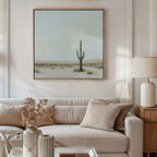 A cozy living room with a beige sofa, neutral cushions, a lamp, and a vase with dried flowers. Above the sofa hangs the Saguaro Whisper Canvas Art—a minimalist print of a lone saguaro cactus in a tranquil desert landscape.