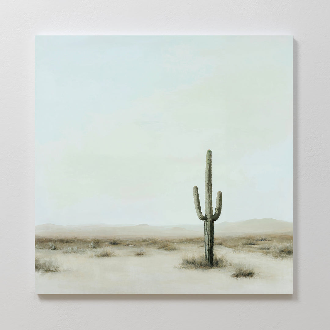 The Saguaro Whisper Canvas Art showcases a tall saguaro cactus in a serene desert landscape with sparse grass and a pale sky, bringing minimalist style and tranquil vibes to any space.