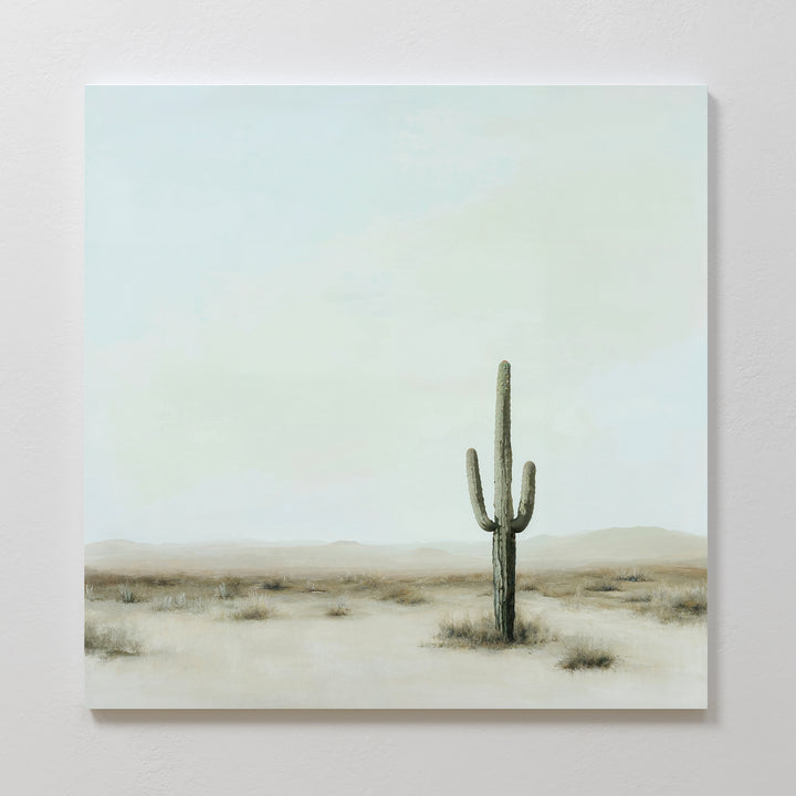 The Saguaro Whisper Canvas Art showcases a tall saguaro cactus in a serene desert landscape with sparse grass and a pale sky, bringing minimalist style and tranquil vibes to any space.