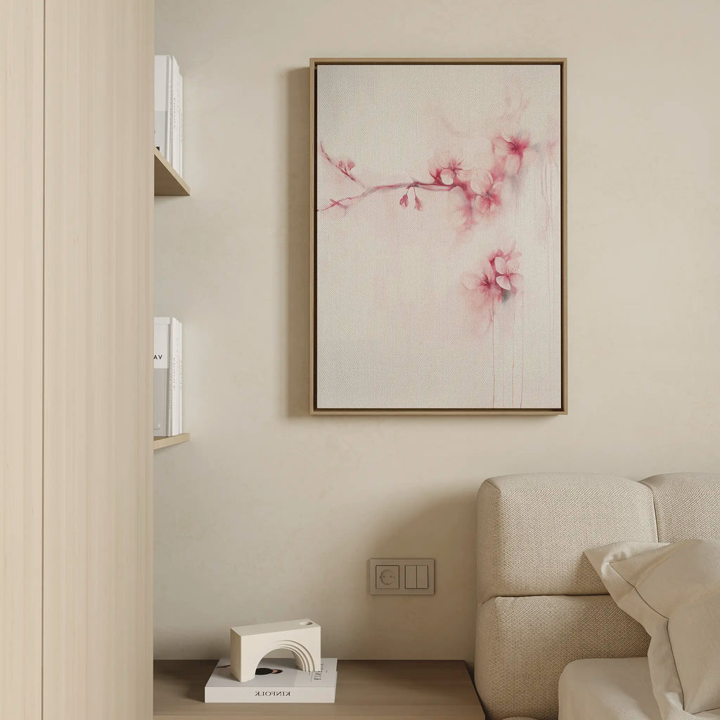 A minimalist living room corner features a light beige sofa, a small bookshelf, and the Sakura Dream Canvas Art, which displays delicate pink flowers on a white background. Neutral tones throughout create a calm, inviting atmosphere.