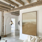 A modern living room with exposed wooden ceiling beams, white walls, Sand and Sea Abstract Canvas Art above the sofa, a curved floor lamp, neutral decor, and natural light filling the space.