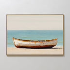 The Sandbound Vessel Canvas Art features a weathered white rowboat on a sandy beach with calm turquoise water and pale sky, framed and displayed on a white wall—ideal for adding serene coastal style to any bedroom.
