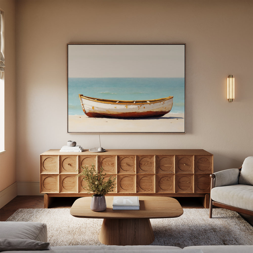 A cozy living room with neutral tones, featuring a wooden sideboard, low coffee table, light sofa, and the Sandbound Vessel Canvas Art—a coastal boat scene—above the sideboard. A small vase with flowers sits on the table.