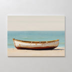 Sandbound Vessel Canvas Art features a white, weathered rowboat on a sandy beach with a calm blue sea and pale sky—ideal coastal wall art for minimalist decor and creating a tranquil atmosphere in any bedroom.