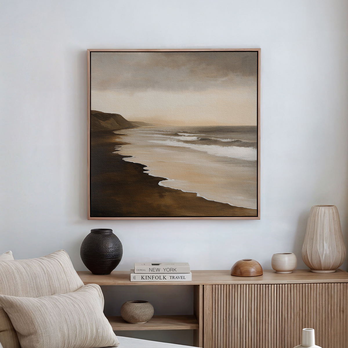 A neutral-toned living room features the Sandy Shoreline Canvas Art above a wooden sideboard, styled with ceramic vases, a lamp, and stacked books. Light beige sofa cushions bring extra warmth to this inviting space.