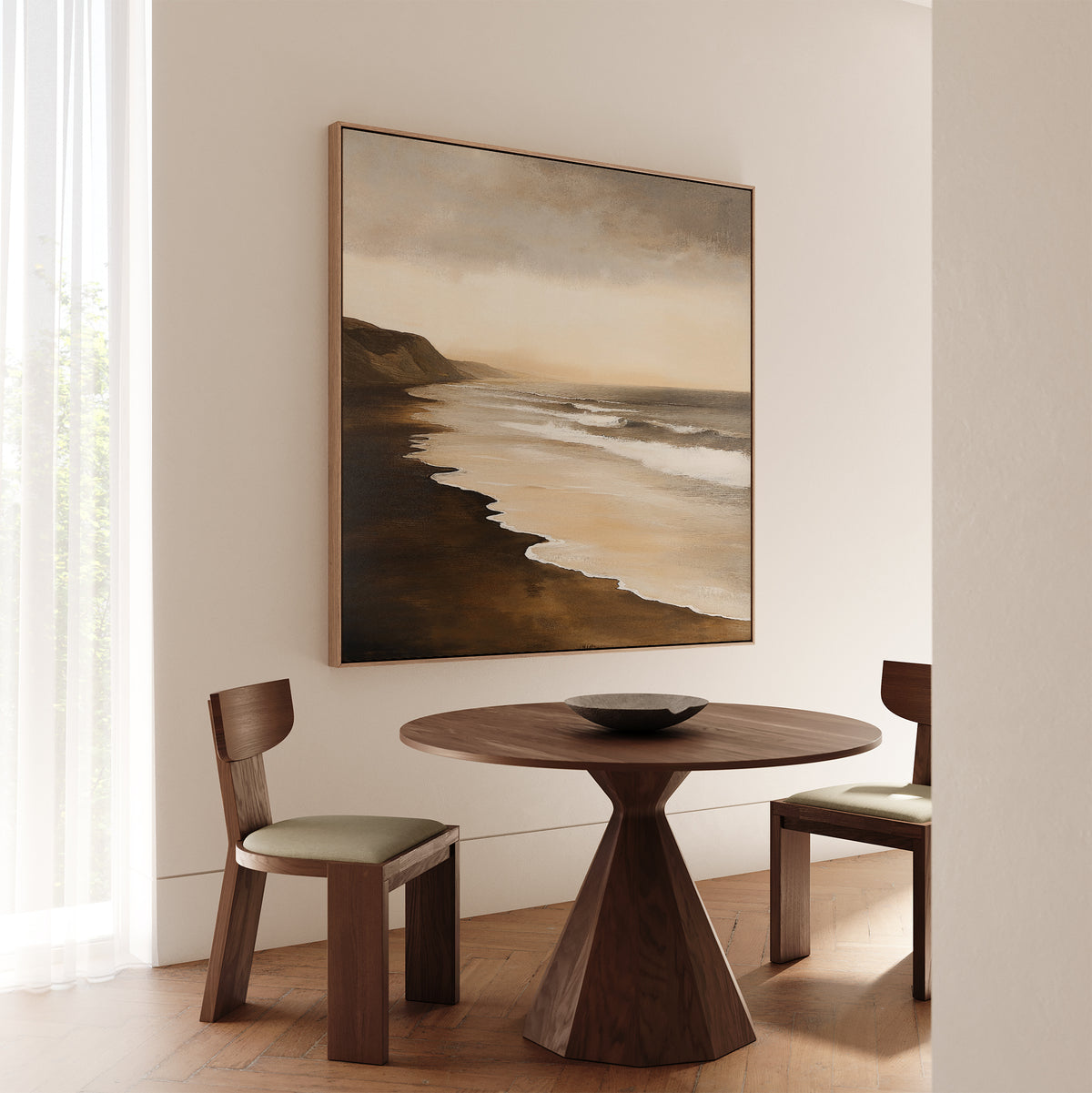 A minimalist dining area with two wooden chairs and a round table sits beneath the Sandy Shoreline Canvas Art. Soft natural light filters through sheer curtains, creating an inviting space perfect for relaxing living room decor.