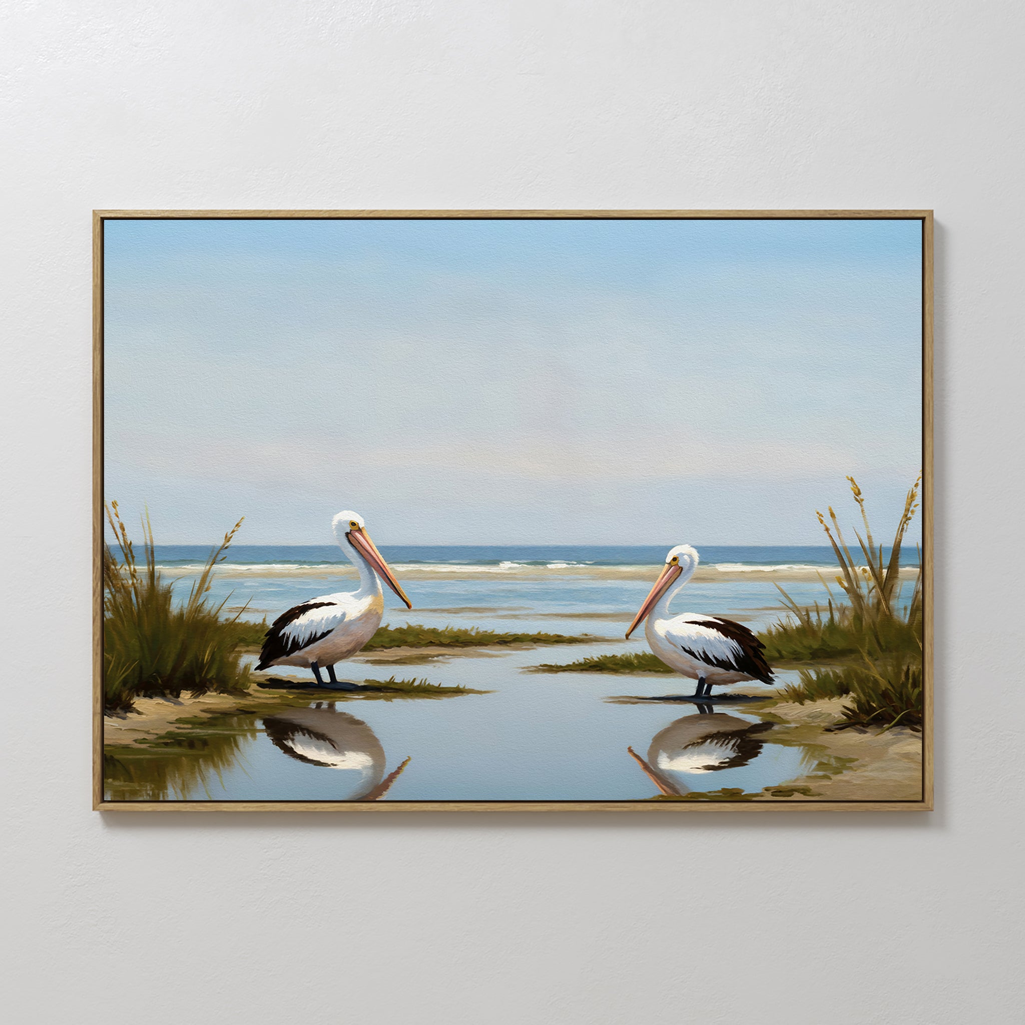 Seaside Gaze Canvas Art: A framed coastal print showcasing two pelicans by the water amid grass, with the ocean and blue sky mirrored on the calm surface—a serene touch for your decor.