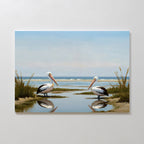 Seaside Gaze Canvas Art features two pelicans by the water among tall grasses, their reflections mirrored in the calm surface beneath a blue sky—perfect for adding coastal serenity to your space.