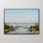 The Seaside Gaze Canvas Art features two pelicans by the water amid grassy banks, their reflections shimmering beneath a blue sky and ocean—ideal coastal wall decor for any room.