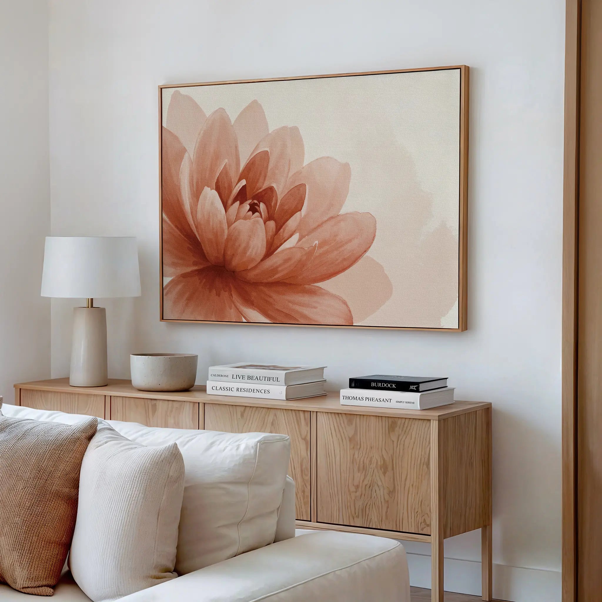 A modern living room features a light wood sideboard, neutral decor, a white table lamp, books, and the Sepia Lotus Canvas Art with a soft peach-toned flower. A cream sofa sits in the foreground.