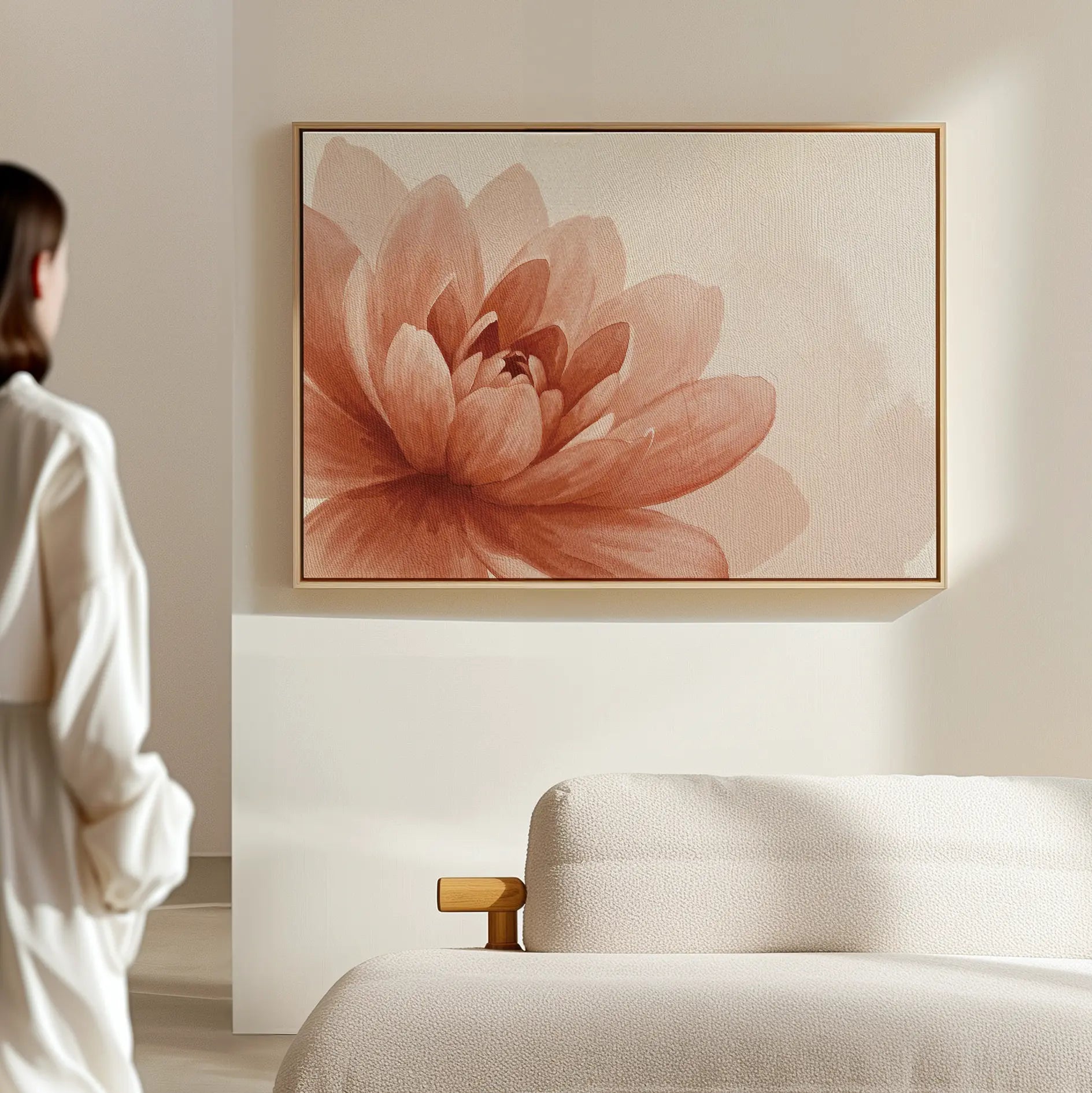 A woman in a white robe stands by a light sofa in a modern living room, admiring the Sepia Lotus Canvas Art featuring a soft, pinkish-orange flower and minimalist floral design.