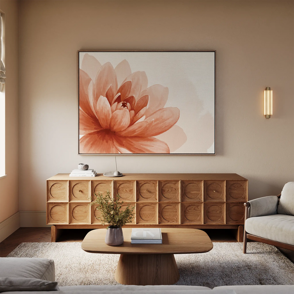 A cozy living room with a light gray sofa, wooden coffee table, and sideboard with circular patterns. Above the sideboard, Sepia Lotus Canvas Art in peach tones adds charm. A small plant and books rest on the table.