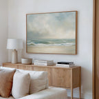 A modern living room with a wooden sideboard, stacked books, a white lamp, and neutral décor. Above the sideboard, a large framed Serene Beach Canvas Art adds calming vibes to the space.