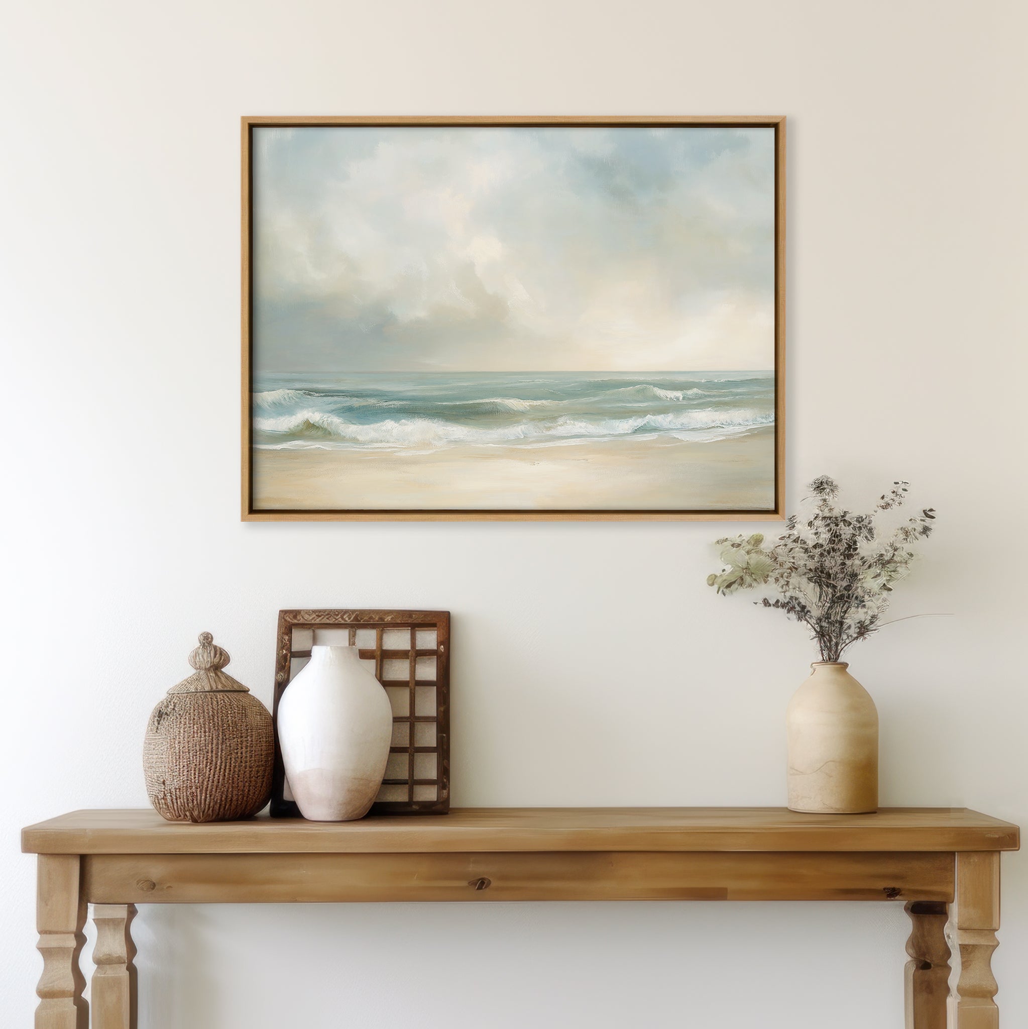 A wooden console table with decorative vases and dried flowers sits beneath a framed Serene Beach Canvas Art on a light-colored wall, creating a tranquil and minimalist coastal decor vibe.