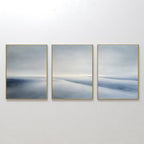 The Serene Horizons Set of 3 features framed abstract paintings with soft, blurred shades of blue, gray, and white on a white wall—evoking a tranquil landscape and adding a calming, expansive touch to any space.