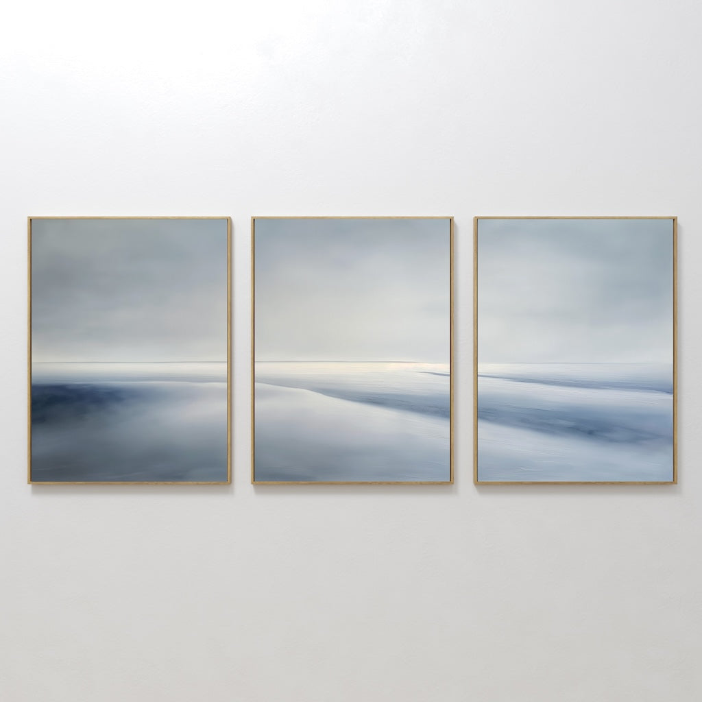 The Serene Horizons Set of 3 features framed abstract paintings with soft, blurred shades of blue, gray, and white on a white wall—evoking a tranquil landscape and adding a calming, expansive touch to any space.