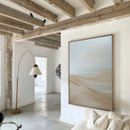 A modern living room with exposed wooden ceiling beams, white walls, a white sofa, a curved floor lamp, and the Serene Peaks Abstract Canvas Art. Natural light streams in through windows in the background.