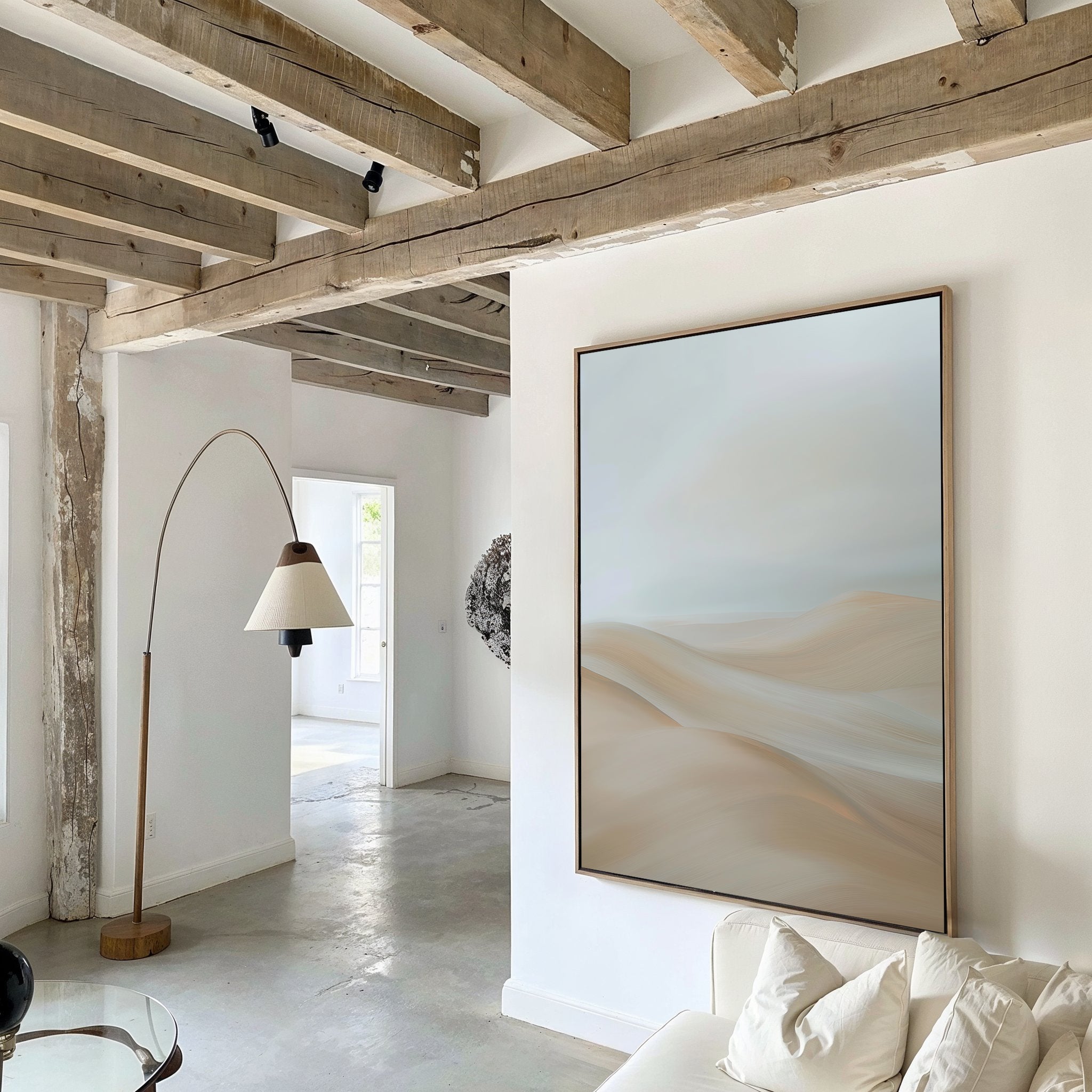 A modern living room with exposed wooden ceiling beams, white walls, a white sofa, a curved floor lamp, and the Serene Peaks Abstract Canvas Art. Natural light streams in through windows in the background.