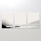 The Serenity Peaks Set of 3 features minimalist, monochrome landscape paintings with soft black, gray, and white gradients depicting foggy mountains and tranquil water in a modern style, perfect for a serene wall display.