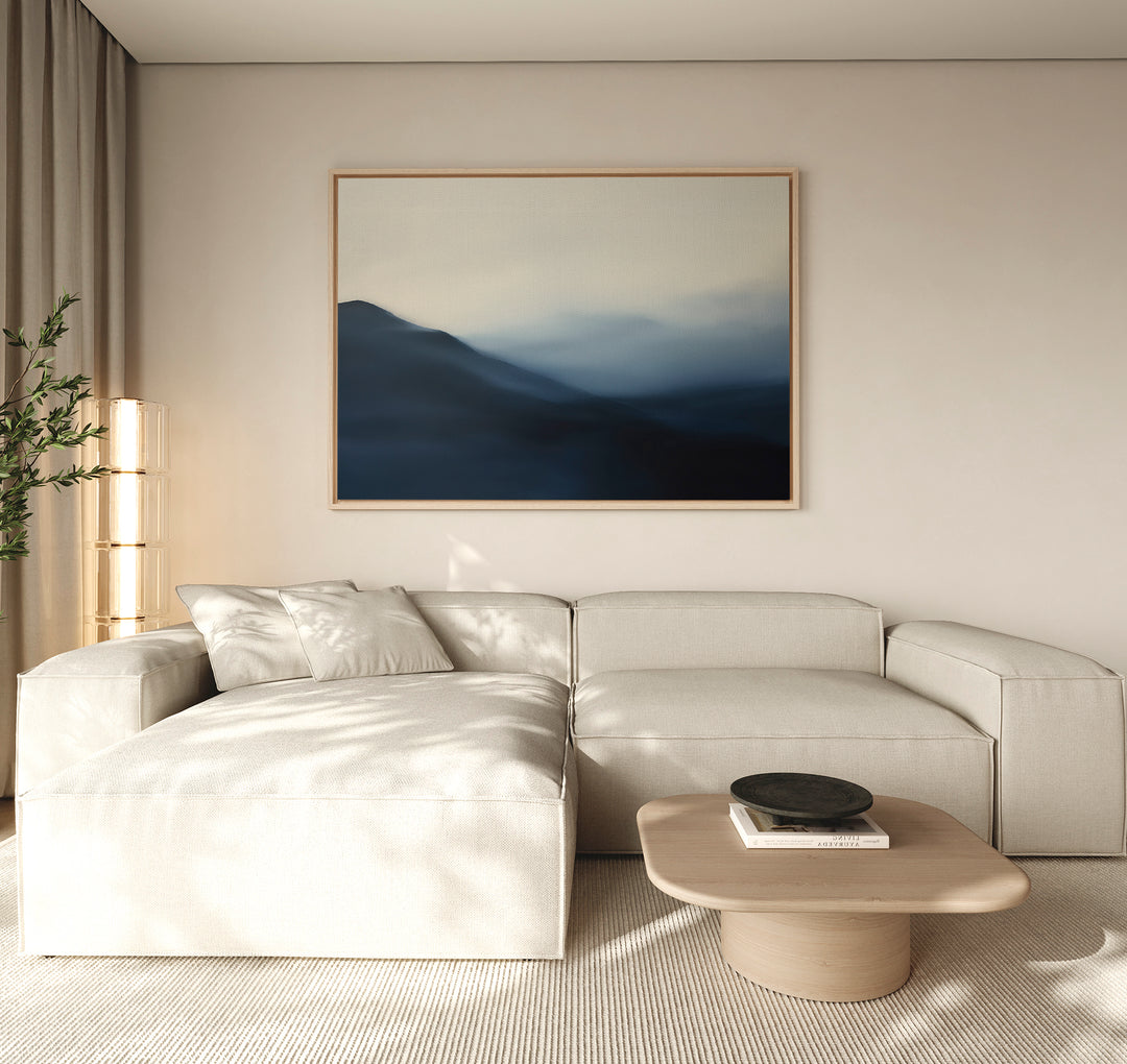 A modern living room with a beige sectional, light wood coffee table, minimal floor lamp, and the Shadowed Valley Canvas Art – Horizontal. Neutral tones and soft natural light create a serene, minimalist atmosphere.
